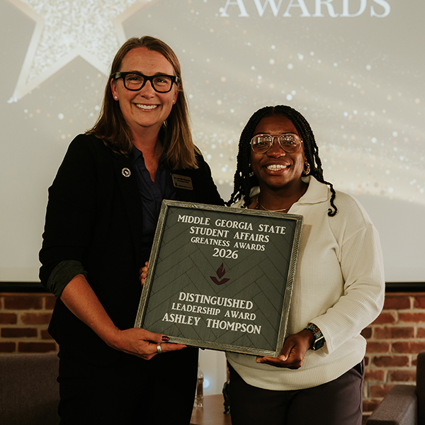 XDr. Jennifer Brannon and award recipient Ashley Thompson smile while holding a plaque that reads, "Middle Georgia State Student Affairs Greatness Awards 2026 - Distinguished Leadership Award, Ashley Thompson."
